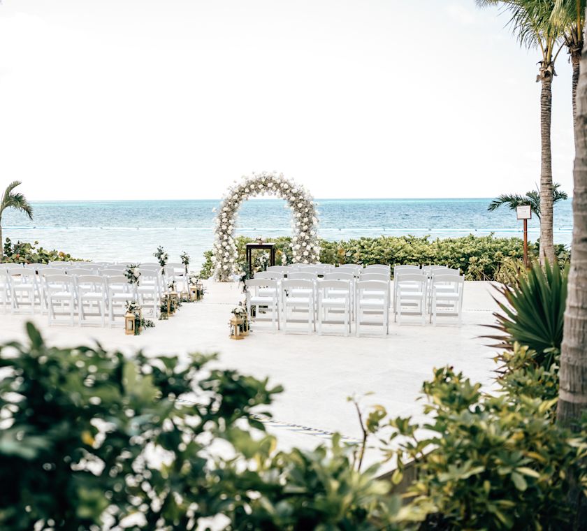 beach wedding ceremony set up with chairs and a flower arch