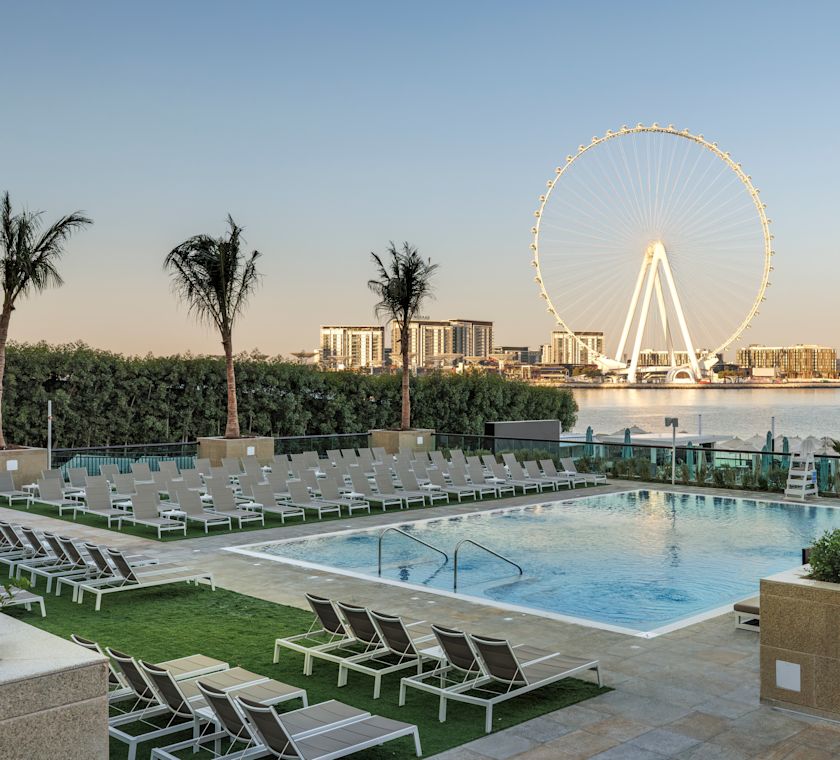 Outdoor pool with surrounding loungers and ferris wheel