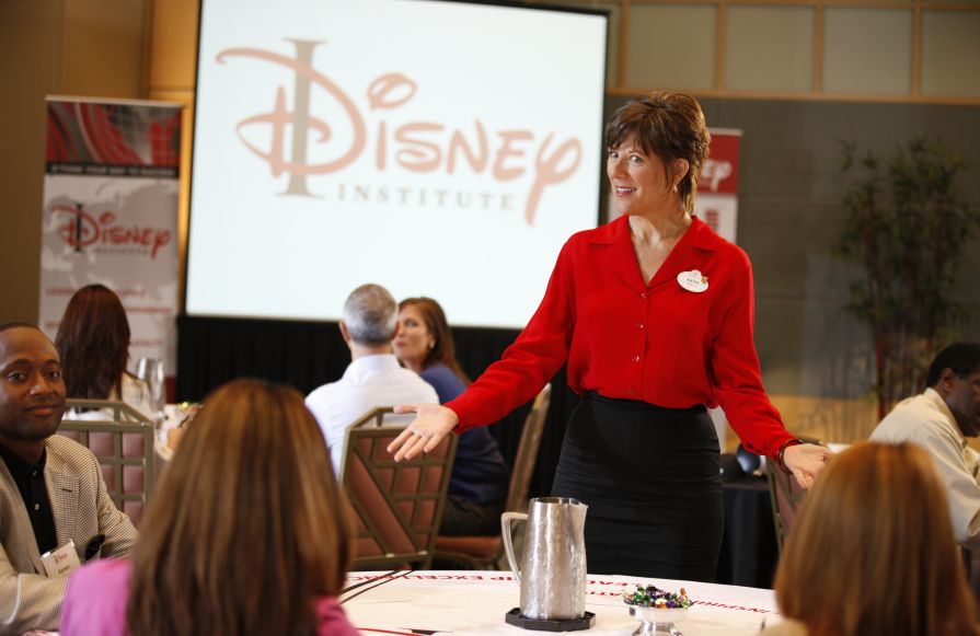 Gambar gaya hidup Disney Institute wanita mengenakan kemeja merah berbicara dengan orang-orang-transisi