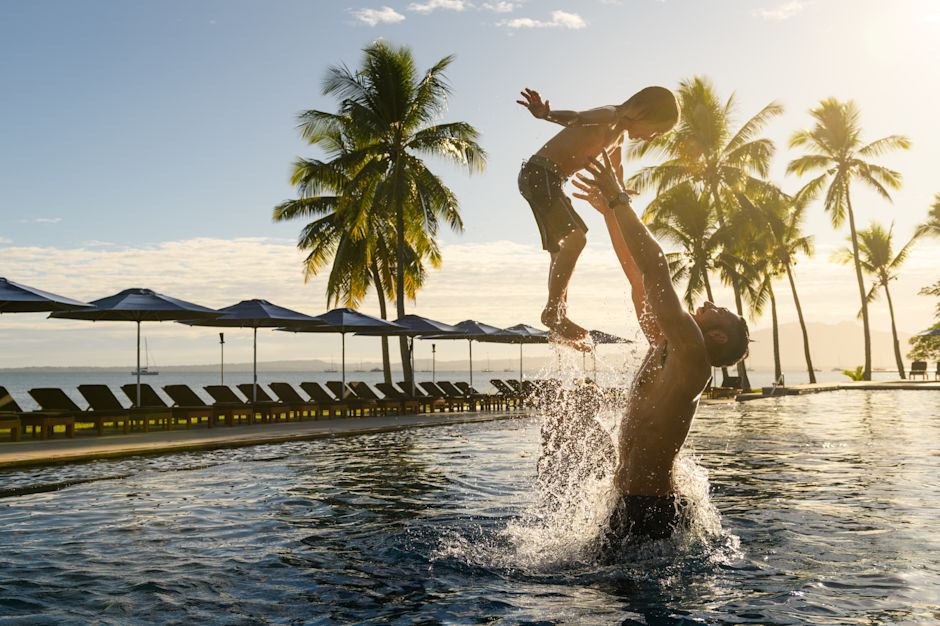 A man throwing his son in the air, while playing in the main pool.