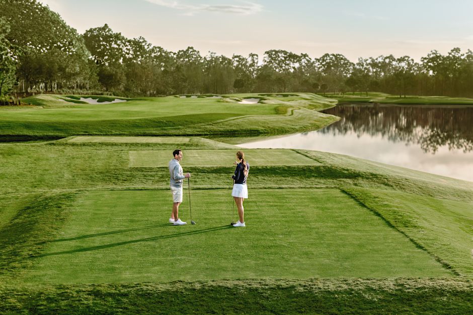 Un homme et une femme debout sur un terrain de golf avec un danger aquatique et des arbres