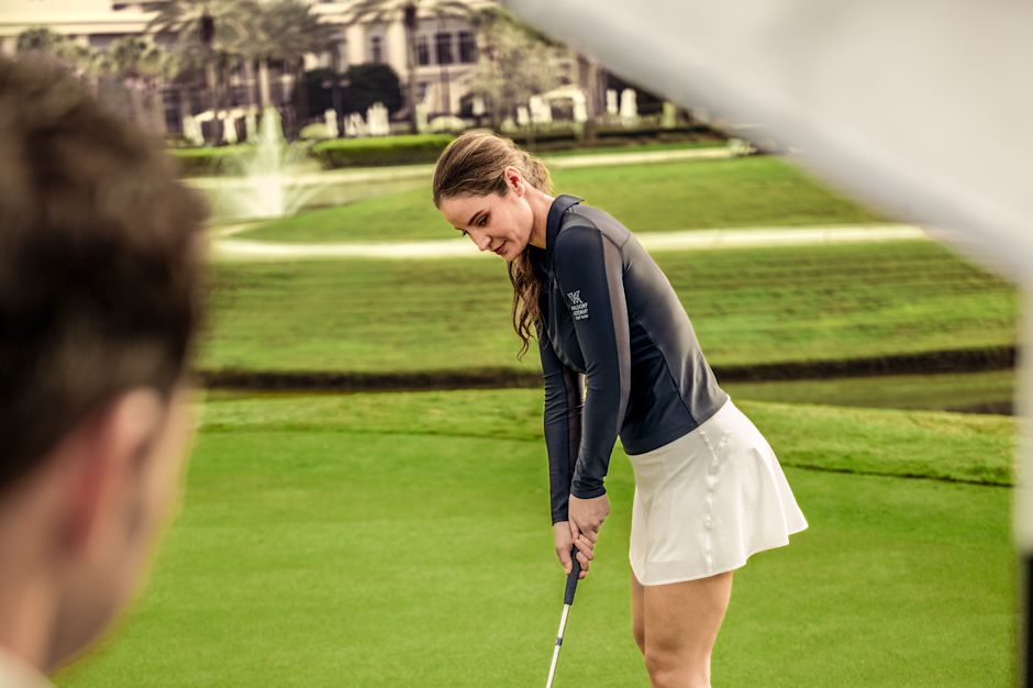 Femme en train de faire la queue sur le green du parcours de golf alors qu'un homme tient un drapeau