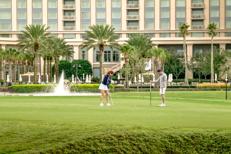 Un homme et une femme sur un putting green, une femme tirant une balle alors qu'un homme tient le drapeau