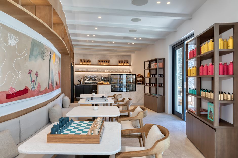 Stari Bakery seating area with a long bench and tables, as well as shelves with water bottles for sale, and a coffee service counter in the background.-transition