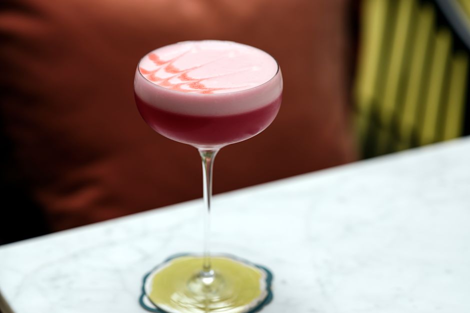 A pink cocktail with foam in a coupe glass on a marble table
