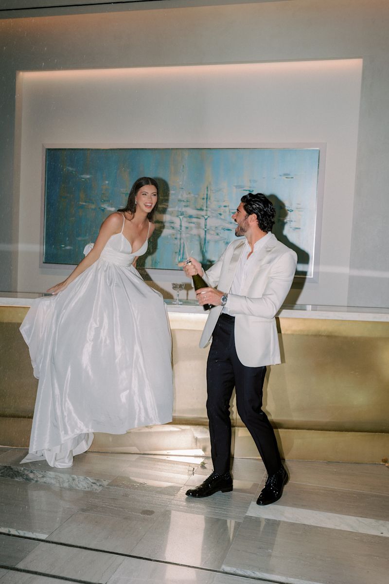 Bride and groom popping a bottle of champagne at reception.