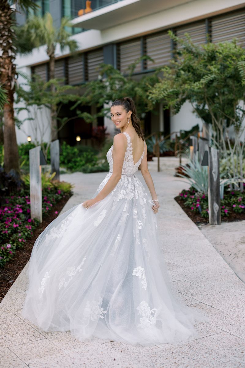Bride in wedding gown looking back over her left shoulder while she is walking on concrete pathway through the gardens.