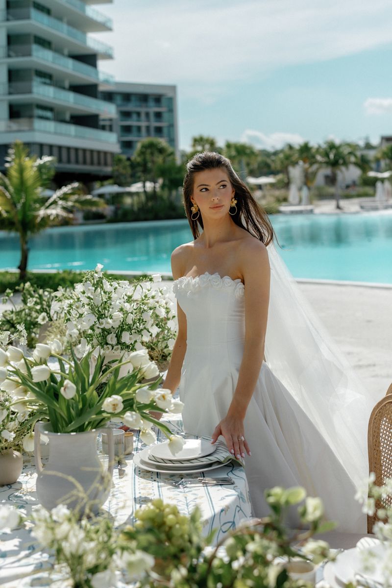 Une mariée debout autour d'une table avec des épices centrales florales et prête pour un dîner dans un cadre extérieur élégant.