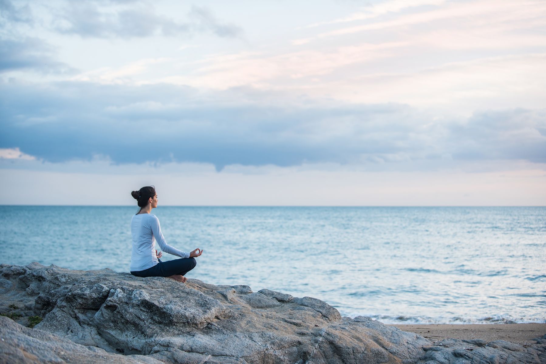 Femme en train de méditer sur un rocher en regardant la mer à l'aube