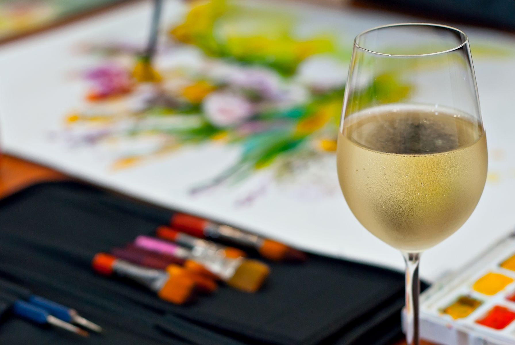 Wine glass with paints and canvas in the background