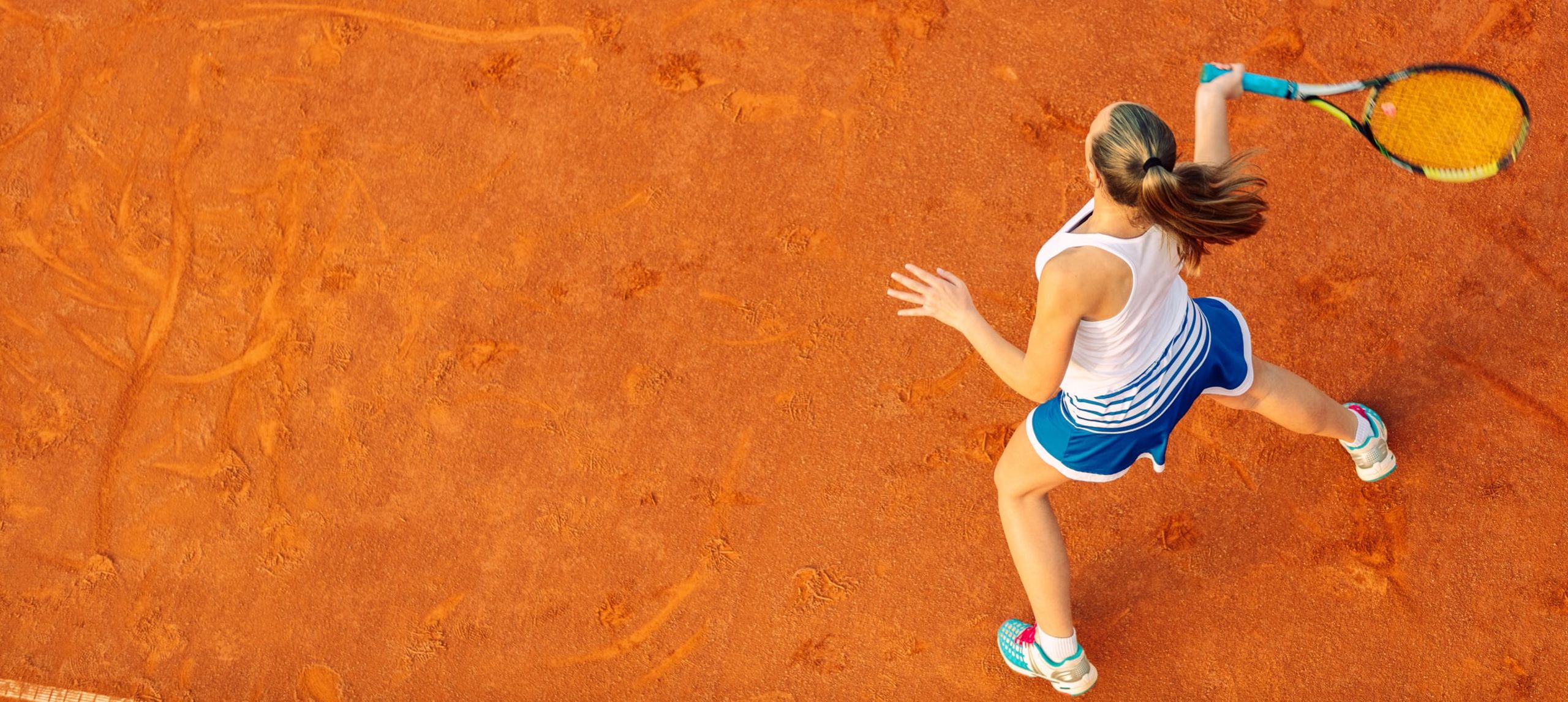 Girl playing tennis on red tarmac