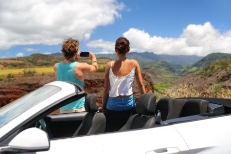 Couple standing next to a convertible car taking a picture of Hawaii scenery