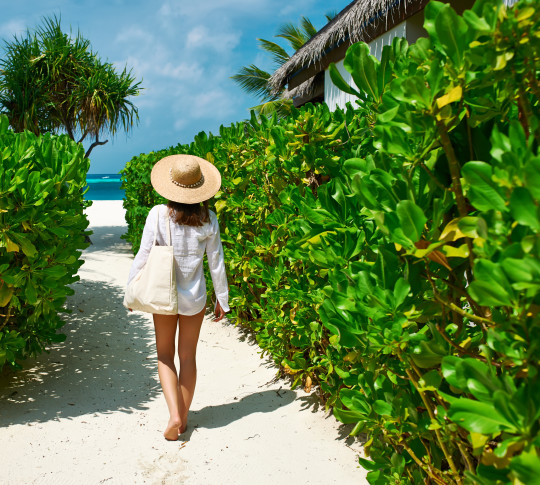 Lady walking through a hedged pathway towards a beach.