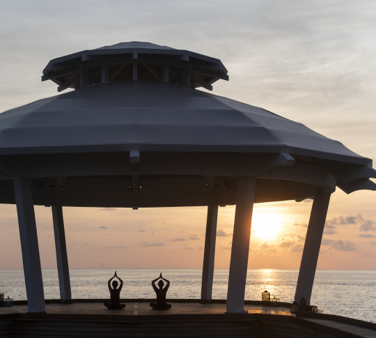 Two people in the Ocean Pavilion at sunset doing yoga