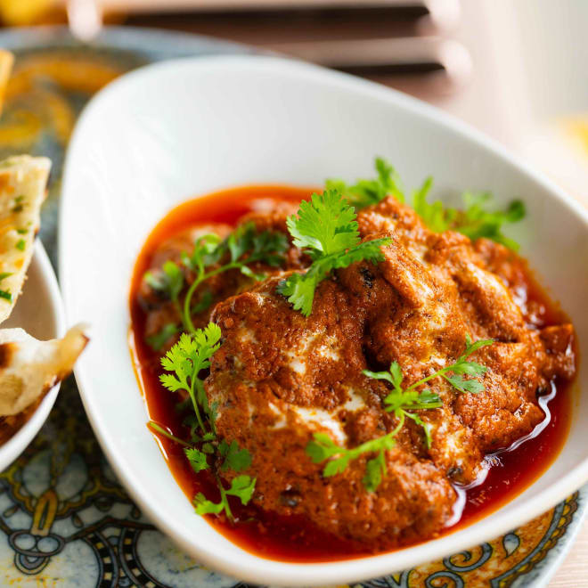 Pain Naan légèrement grillé dans un panier à côté d'un plat de curry assaisonné