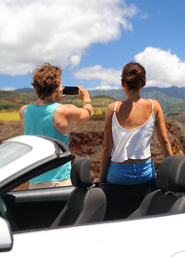 Pariskunta seisomassa muunneltavan auton vieressä ottamassa kuvaa Havaijin maisemista