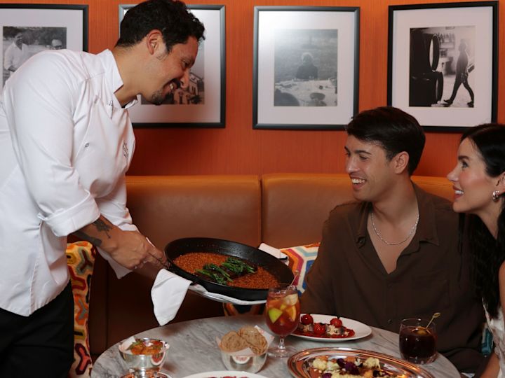 José by Pizarro, server care le oferă oaspeților un vas de paella