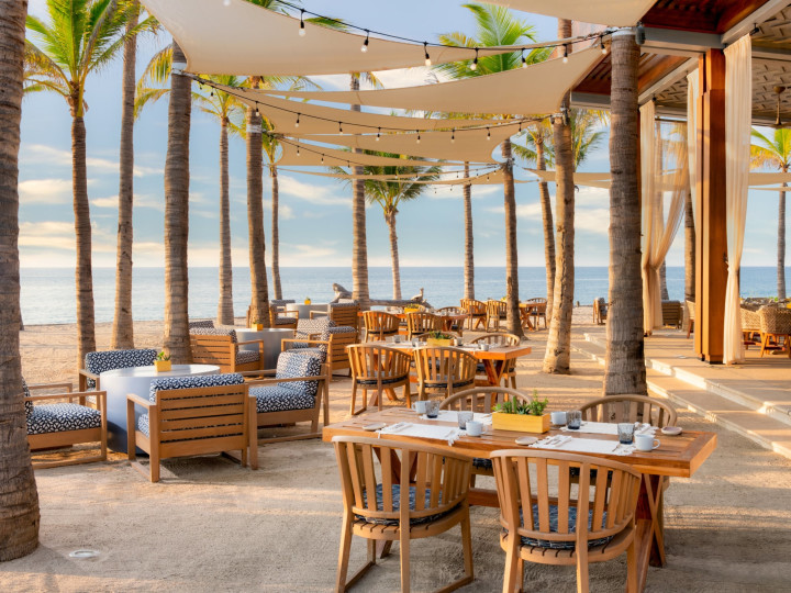 Restaurant with tables and chairs and palm trees and beach in background