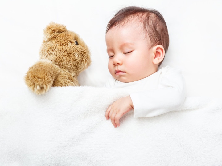 A baby peacefully sleeping tucked in with their teddy bear.