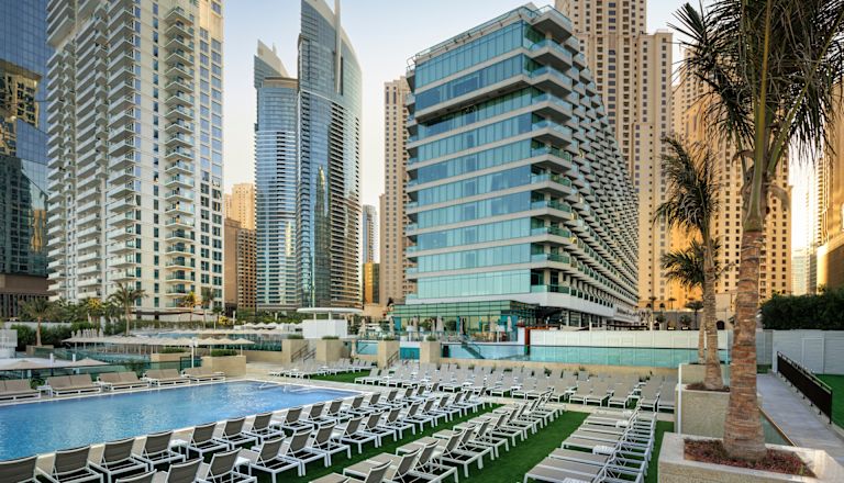 Hotel exterior with outdoor pool and rows of loungers